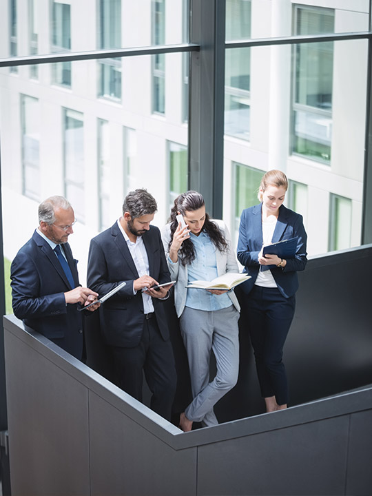 Vier Fachleute in einem modernen Bürogebäude, die mit Smartphones und Notizbüchern arbeiten