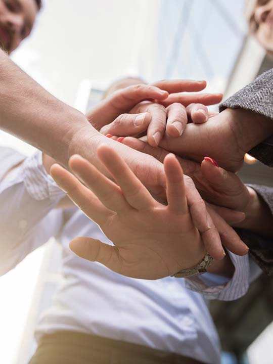 Hände von mehreren Personen übereinander, die Zusammenarbeit und Teamarbeit symbolisieren